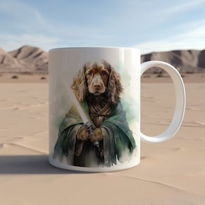 Puede incluir: Taza de cerámica blanca con una ilustración en acuarela de un perro Cocker Spaniel vestido de Jedi, sosteniendo un sable de luz brillante. El perro tiene pelaje marrón y lleva una túnica verde. El fondo muestra un paisaje desértico.