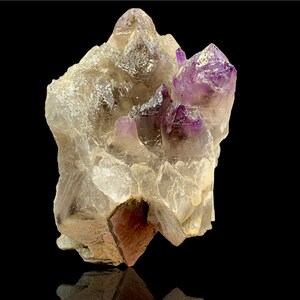 Könnte beinhalten: Ein Cluster aus Amethystkristallen mit einer klaren Quarzmatrix. Die Amethystkristalle sind tiefviolett und haben eine spitze Form. Die Quarzmatrix ist klar und hat eine raue Textur.