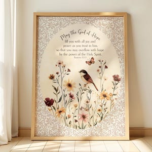 Könnte beinhalten: Gerahmter Kunstdruck mit floralem Design, Vogel und Schmetterling. Der Druck enthält den Text "May the God of Hope" und einen Bibelvers. Der Rahmen ist hellbraun.