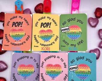 Könnte beinhalten: Fünf bunte Valentinstagskarten mit Pop-it-Fidget-Spielzeug. Jede Karte zeigt ein Regenbogen-Pop-it-Herz mit einem lächelnden Gesicht und dem Text "You make my heart POP!" oder "Just popping in to say happy Valentine's Day!" oder "So glad you popped into my life!" mit dem Absendernamen "KORI".