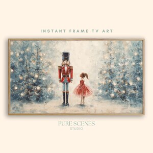 Op de afbeelding: Een ingelijste digitale kunstprint met een notenkraker en een meisje in een rode jurk in een besneeuwd bos met kerstbomen. De tekst "INSTANT FRAME TV ART" staat bovenaan. Het kunstwerk is van PURE SCENES STUDIO.