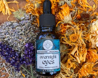 May include: A dark glass dropper bottle labeled Earthshine Medicinals overnight eyes herbal makeup remover 0.5 fluid oz, surrounded by dried orange calendula petals and purple lavender sprigs.