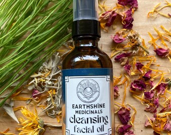 May include: A brown glass bottle of Earthshine Medicinals cleansing facial oil with a black pump top. The label features a sun and moon design. Dried flowers and greenery surround the bottle. The bottle contains 2 fluid ounces.