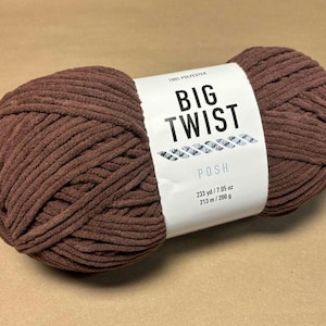 Puede incluir: Una gran madeja de hilo marrón con una etiqueta blanca. La etiqueta dice "BIG TWIST POSH" e indica la longitud y el peso del hilo como 213 metros / 200 gramos. El hilo es 100% poliéster. La madeja es de color marrón.