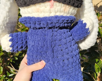 May include: A crocheted plush toy rabbit wearing a blue jumpsuit and a black eye mask. The rabbit has white fur and long floppy ears.