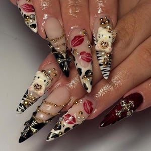 Puede incluir: Una manicura con u&ntilde;as acr&iacute;licas largas y puntiagudas con varios dise&ntilde;os. Algunas u&ntilde;as presentan un dise&ntilde;o de Hello Kitty, otras labios rojos y otras un estampado de vaca en blanco y negro. Tambi&eacute;n hay detalles dorados y perlados.
