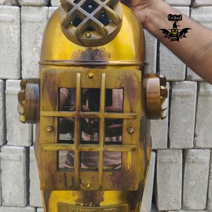 Può includere: Un casco da sub vintage in ottone con un oblò rotondo in vetro trasparente e una placca in ottone con il testo "BRONZE  W.P.  NO. 8 DIVING CO. MILLER - DUFFY CO.  HAVANA, CUBA".