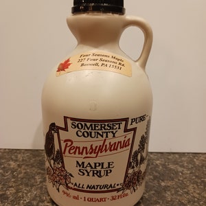 May include: A white plastic jug with a black lid and a red and white label. The label says "Somerset County Pennsylvania Maple Syrup All Natural 946 ml - 1 Quart - 32 fl oz".