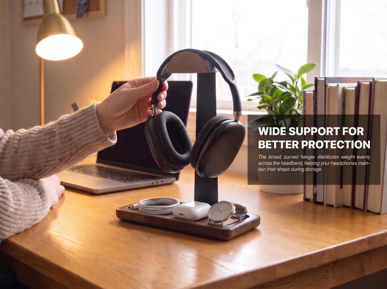 May include: A dark wood headphone stand with a black vertical support and a curved top hanger. The base features a tray holding a white charging cable, white wireless earbuds in a case, and a silver wristwatch. Text reads: WIDE SUPPORT FOR BETTER PROTECTION.