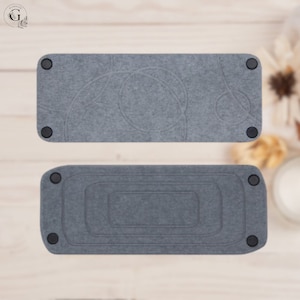 May include: Two gray felt trays with rounded corners and black rubber feet. The top tray has a circular design, while the bottom tray has a rectangular design. The trays are shown from two different angles.