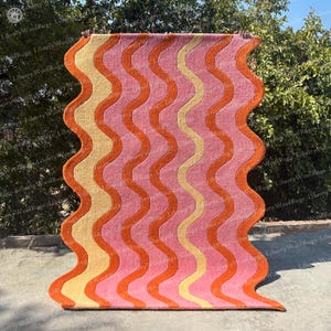 May include: A wavy patterned rug with pink, orange and yellow stripes. The rug is made of wool and has a modern design.