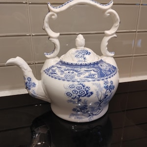 Peut inclure: Une théière en céramique blanche ornée d'un motif floral bleu complexe sur le corps et le couvercle. La théière présente un bec verseur incurvé et une anse décorative et ornée avec des accents bleus. Un petit bouton pointu surmonte le couvercle.