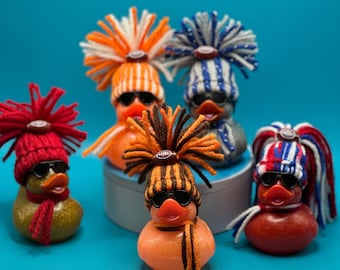 May include: Five rubber duckies with different colored hats and designs. The ducks are all wearing hats with different colors and patterns, including red, white, blue, and black. The ducks are all sitting on a white surface.