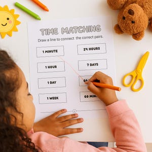 May include: A child is drawing on a "Time Matching" worksheet with an orange crayon. The worksheet has time-related terms to match. A yellow pair of scissors, a plush teddy bear, and crayons are on the white surface.
