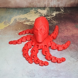 Puede incluir: Un pulpo rojo impreso en 3D con una cabeza de Deadpool. El pulpo tiene ocho tentáculos y está hecho de un material plástico liso.