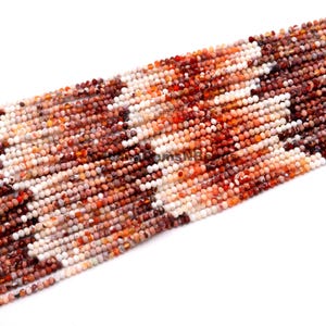 May include: Strands of small, faceted beads in shades of white, orange, and brown. The beads are strung together, creating a textured surface. The beads are likely for jewelry making.