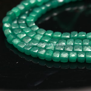 May include: A strand of green faceted gemstone beads. The beads are square shaped and have a smooth, polished finish.
