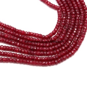 Puede incluir: Una hebra de cuentas de piedras preciosas facetadas de color rojo intenso. Las cuentas son pequeñas y redondas, y están enhebradas en un hilo transparente. Las cuentas están dispuestas en un patrón suelto y fluido.