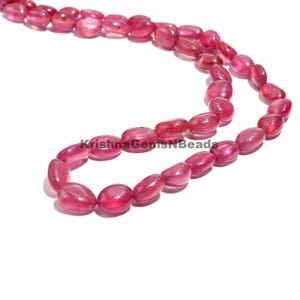 Puede incluir: Un collar de piedras preciosas rosas, pulidas y de forma ovalada. Las cuentas están ensartadas. La imagen incluye el texto "KrishnaGemsNBeads".