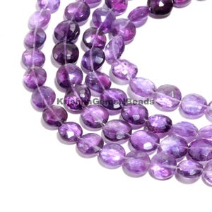 Peut inclure: Gros plan sur des brins de perles d'améthyste facettées. Les perles sont de forme ovale et de couleur violet foncé, avec des inclusions violet clair et blanches. Le texte "KrishvaGemsNBeads" est visible. Les perles sont enfilées, prêtes pour la création de bijoux.