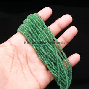 Puede incluir: Una colección de pequeñas y vibrantes cuentas de piedras preciosas verdes. Las cuentas están ensartadas, creando múltiples hebras. El texto "Krishna Gems n Beads" es visible. Las cuentas se sostienen en una mano sobre un fondo negro.