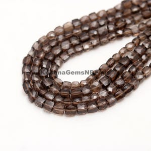 Puede incluir: Una hebra de cuentas de cuarzo ahumado, cada cuenta está facetada y tiene forma cuadrada. Las cuentas están enhebradas en un hilo transparente y están dispuestas en un patrón suelto y fluido.