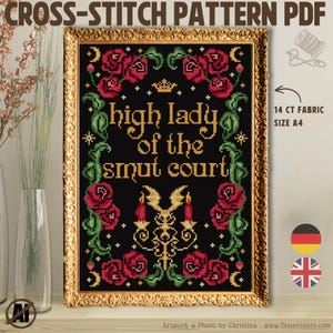 May include: A framed cross-stitch pattern with the text "high lady of the smut court" in gold lettering. The design features red roses, green vines, and a gold candelabra on a black background. The frame is gold.