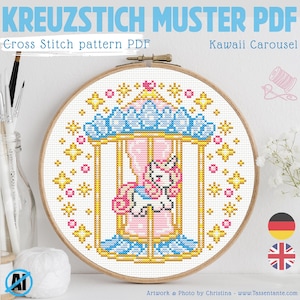 Puede incluir: Un patrón de punto de cruz en un aro de madera presenta un diseño de carrusel con un unicornio. El diseño incluye elementos azules, rosas y dorados, con el texto "KREUZSTICH MUSTER PDF" y "Cross Stitch pattern PDF".