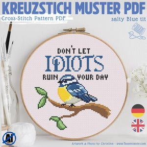 Peut inclure: Un modèle PDF de point de croix avec un motif d'oiseau mésange bleue sur une branche, avec le texte "DON'T LET IDIOTS RUIN YOUR DAY". Présenté dans un cercle à broder en bois.