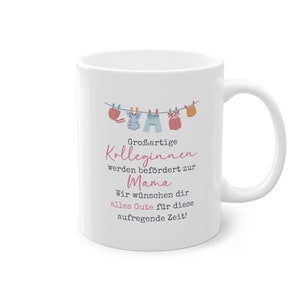 May include: White ceramic mug with a design of clothes hanging on a clothesline. The text reads "Großartige Kolleginnen werden befördert zur Mama. Wir wünschen dir alles Gute für diese aufregende Zeit!"