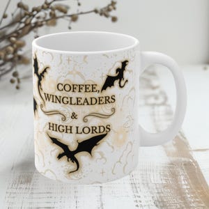 Könnte beinhalten: Weiße Keramik-Kaffeetasse mit einem schwarz-weißen Design mit Drachen und dem Text "Coffee, Wingleaders & High Lords".