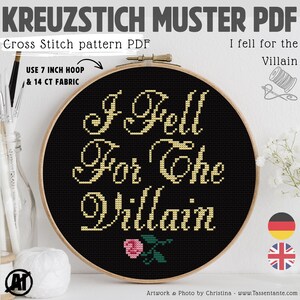 Op de afbeelding: Een kruissteekpatroon PDF in een houten hoepel. Het ontwerp toont de tekst "I Fell For The Villain" in gouddraad op een zwarte achtergrond, met een kleine roze roos. De tekst "Cross Stitch pattern PDF" is ook zichtbaar.