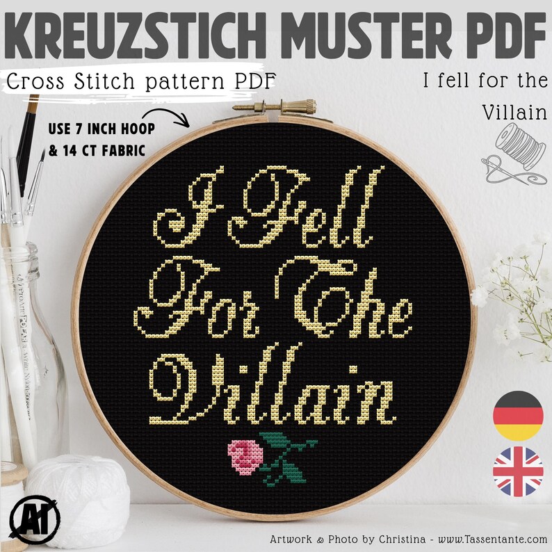 Op de afbeelding: Een kruissteekpatroon PDF in een houten hoepel. Het ontwerp toont de tekst "I Fell For The Villain" in gouddraad op een zwarte achtergrond, met een kleine roze roos. De tekst "Cross Stitch pattern PDF" is ook zichtbaar.