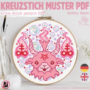 Könnte beinhalten: Ein Kreuzstichmuster-PDF in einem Holzrahmen. Das Design zeigt einen rosa Cartoon-Dämon mit Flammen und Blasen. Der Text lautet "KREUZSTICH MUSTER PDF" und "Cross Stitch pattern PDF". Der Künstler ist "Bubbly Baphi".