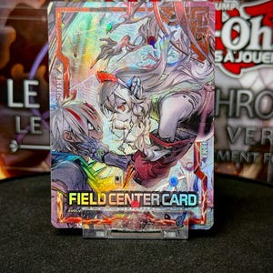 Pode incluir: Um cartão colecionável holográfico com uma ilustração de anime de dois personagens em combate. O cartão tem uma borda rosa e prateada com o texto "FIELD CENTER CARD" e "EVOLV CARDS".
