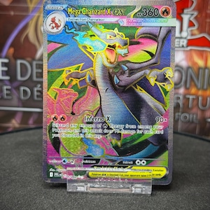 Op de afbeelding: Een holografische Mega Charizard X EX Pokémon-kaart. De kaart toont een draak met blauwe, gele en oranje accenten. De kaart heeft de tekst "Inferno X" en "360 HP". De kaart wordt in een doorzichtige plastic houder gepresenteerd.