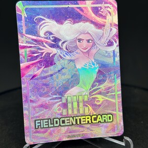 Peut inclure: Une carte holographique avec un design coloré représentant une femme aux longs cheveux blancs et une robe verte et bleue. La carte porte le texte "FIELD CENTER CARD" et "EVOLVE CARDS" imprimé dessus.