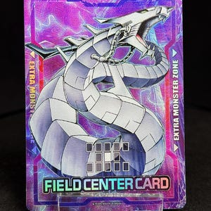 Könnte beinhalten: Eine rechteckige Sammelkarte mit einem silbernen mechanischen Drachen auf einem lila Hintergrund mit Blitzeffekten. Die Karte trägt die Aufschrift "EXTRA MONSTER ZONE" und "FIELD CENTER CARD". Die Karte wird auf einem transparenten Ständer präsentiert.