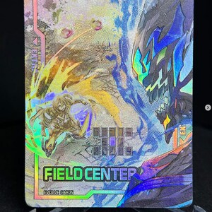 May include: A holographic trading card with a blue and green monster on the right side of the card and a yellow and green character on the left side of the card. The card has the text "FIELD CENTER" and "EVOLVE CARDS" on it.