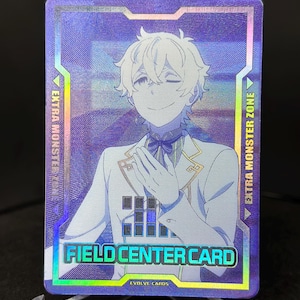 Può includere: Una carta da gioco olografica con un giovane uomo con i capelli bianchi e un abito bianco. La carta ha uno sfondo blu e viola con il testo "FIELD CENTER CARD" e "EVOLVE CARDS".