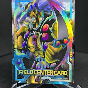 Peut inclure: Une carte de jeu de commerce holographique représentant un monstre violet et vert avec une grande faux. La carte est intitulée "Field Center Card" et "Evolve Cards".