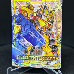 Peut inclure: Une carte de jeu de commerce holographique représentant un robot jaune et bleu avec un robot rouge et jaune en arrière-plan. La carte est intitulée "Field Center Card" et porte la mention "Evolve Cards" en bas. La carte est pour la "Zone Monstre Extra".