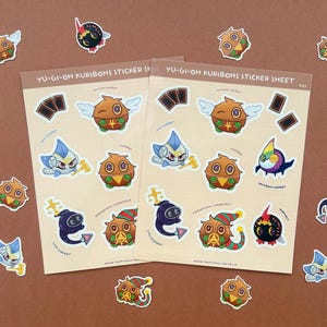 Könnte beinhalten: Zwei Stickerbögen mit verschiedenen Yu-Gi-Oh Kuribohs-Charakteren. Die Bögen haben einen beigefarbenen Hintergrund mit mehreren Aufklebern verschiedener Kuribohs-Designs, darunter geflügelte und gepanzerte Versionen. Einige Aufkleber sind verstreut.