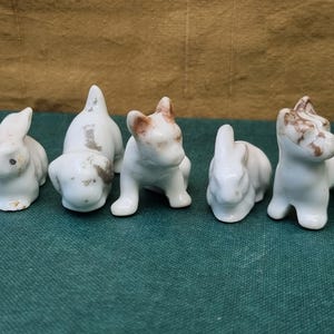May include: Five small, white ceramic animal figurines, including two rabbits and three dogs. The figurines have brown detailing. The animals are arranged in a row, showcasing their detailed features and playful poses.