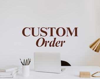 Puede incluir: Un escritorio blanco con un portátil plateado, un portalápices blanco con varios lápices y una pila de libros blancos. La pared sobre el escritorio muestra el texto marrón CUSTOM Order en fuente serif, junto a una lámpara de escritorio dorada.