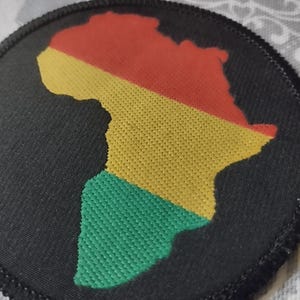 Op de afbeelding: Een zwarte stoffen patch met een gele, rode en groene omtrek van het Afrikaanse continent.