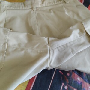 Puede incluir: Primer plano de unos pantalones cortos beige con pu&ntilde;os doblados. Los pantalones cortos tienen un dise&ntilde;o cl&aacute;sico con cierre de bot&oacute;n y cremallera. La tela parece ser un material ligero, adecuado para el clima c&aacute;lido. Los pantalones cortos est&aacute;n cuidadosamente doblados.
