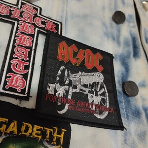Può includere: Una giacca di jeans blu chiaro con diverse toppe di band, tra cui AC/DC, Black Sabbath e Megadeth. La toppa AC/DC presenta un cannone con il testo "For those about to rock, we salute you".