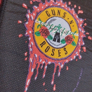 May include: A black fabric patch featuring a red, yellow and white Guns N' Roses logo. The logo is surrounded by a red splatter design.