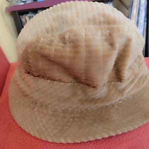 May include: A beige corduroy bucket hat with a wide brim. The hat is made of a soft, textured fabric.
